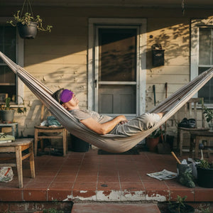 Persona disfrutando de un descanso al aire libre en una hamaca con el antifaz Blackout de Mood Earplugs, bloqueando la luz solar en una terraza en España.