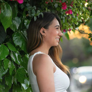Mujer sonriendo en un jardín usando tapones Mood negros para reducir el ruido y el estrés sensorial