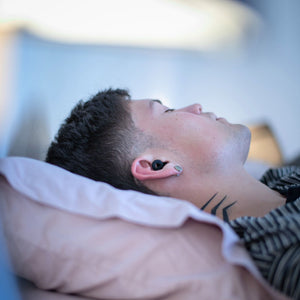 Hombre descansando sobre la cama con los tapones para los oídos reutilizables Mood Earplugs Focus Black, perfectos para aislar el ruido y dormir mejor