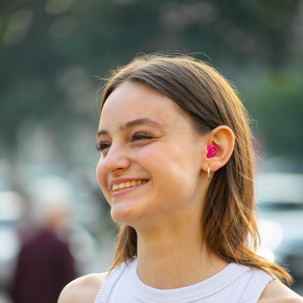 Mujer usando los tapones auditivos Mood Earplugs Pro rosa en un entorno urbano ruidoso, con diseño discreto y ergonómico