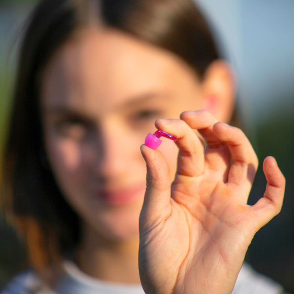 Mujer mostrando en primer plano los tapones auditivos profesionales Mood Earplugs Pro rosa, con máxima atenuación de 38 dB para entornos ruidosos