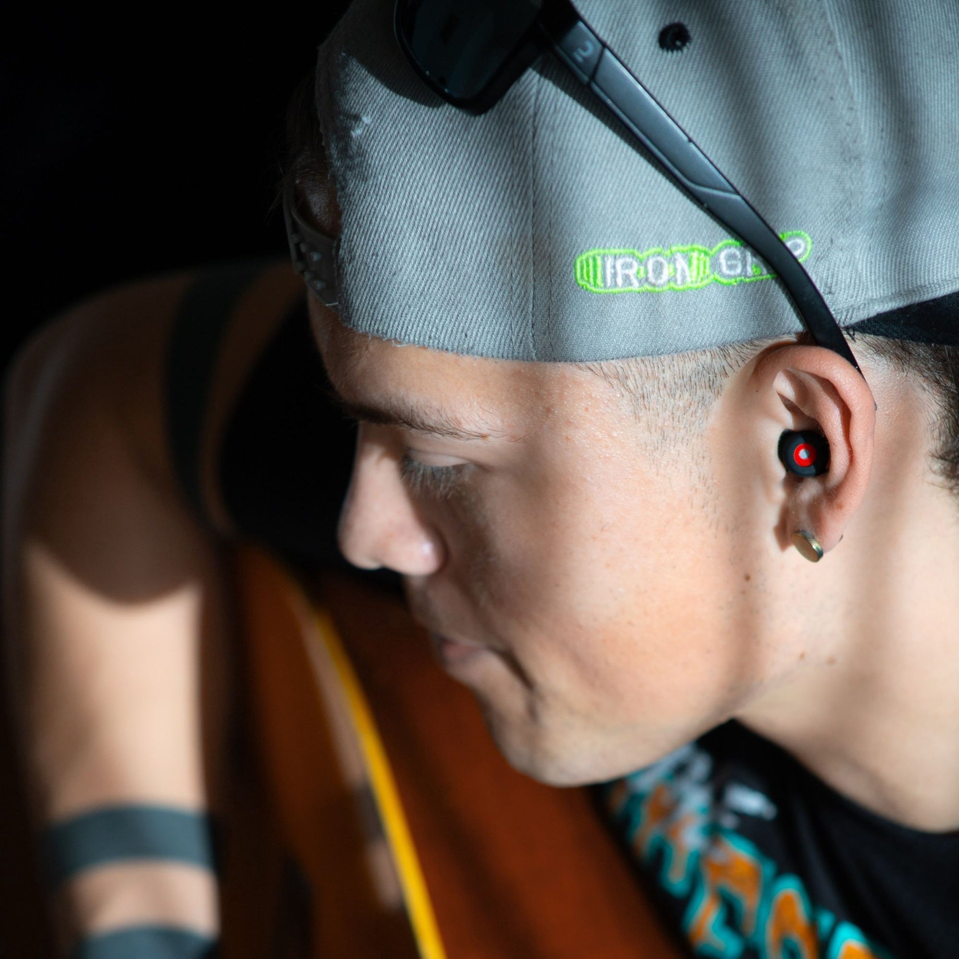Músico con gorra usando los tapones para los oídos reutilizables Mood Earplugs Happy Black mientras toca la guitarra, vista lateral.