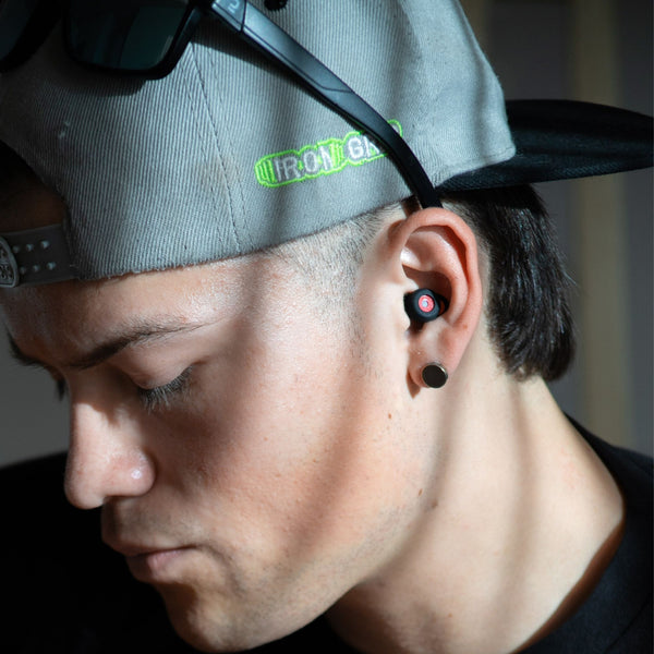 Músico con gorra y tapones para los oidos Mood Earplugs modelo Happy de color Black en primer plano, enfocado en tocar la guitarra