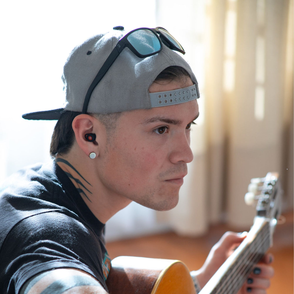 Músico tocando la guitarra con luz natural y usando los tapones para los oídos reutilizables Mood Earplugs Happy Black.