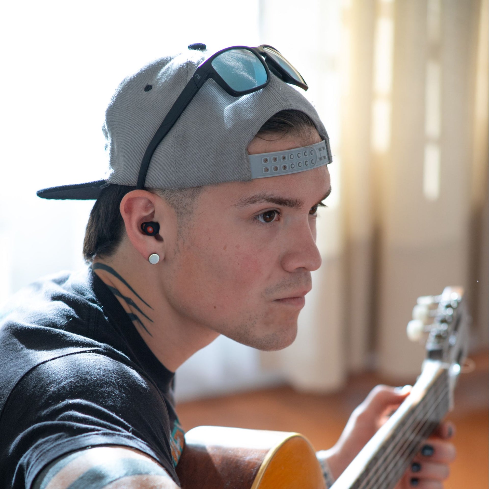 Músico tocando la guitarra con luz natural y usando los tapones para los oídos reutilizables Mood Earplugs Happy Black.